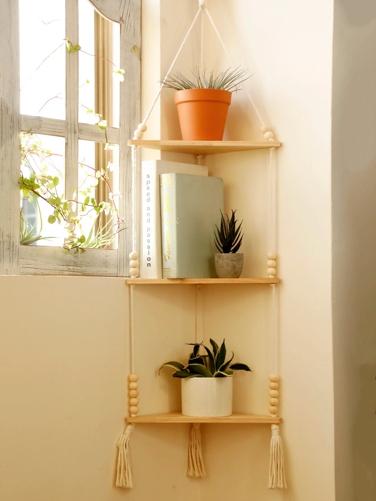 A boho triangle floating wall shelf displaying potted greenery and books against a light wall.