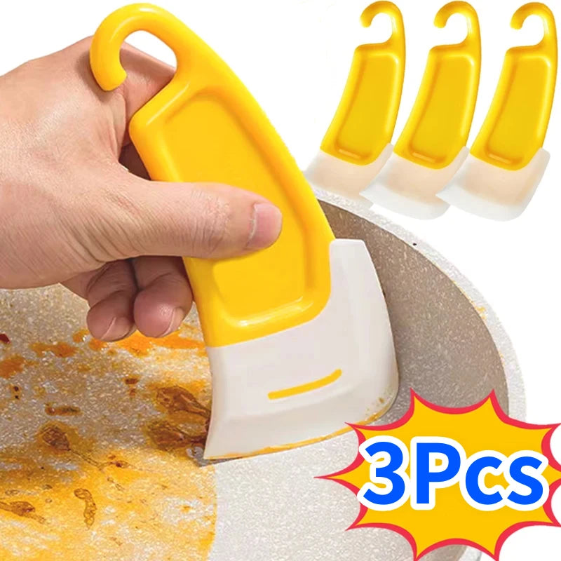 A hand is holding a yellow silicone kitchen scraper set with three pieces on a round surface.