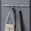 A set of self-adhesive curtain rod hooks is mounted on a silver rod, with a light-colored purse and a gray towel hanging near