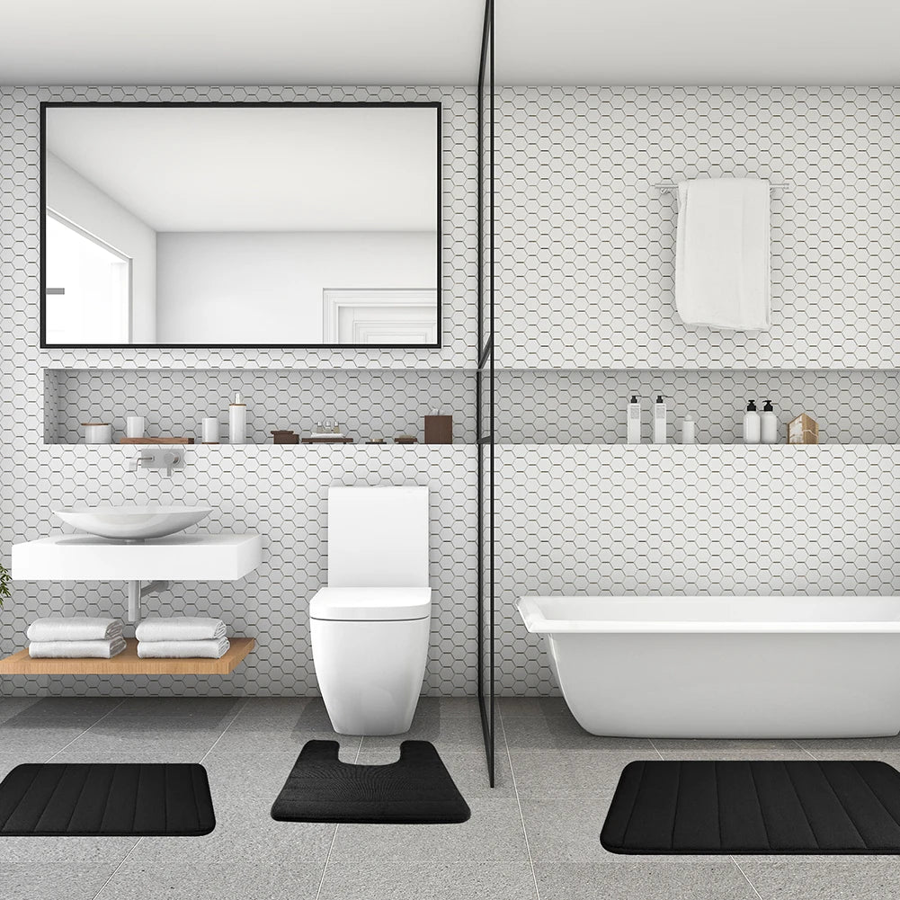 Weiβes Badezimmer mit Toilette, Waschbereich und Badewanne mit schwarzen Memory-Foam-Bodenmatten.
