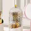 A clear, faceted glass organizer for makeup brushes with a gold lid displayed on a white surface.