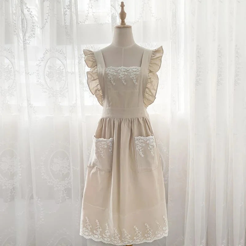 A cream linen kitchen apron with lace detailing and ruffled sleeves displayed on a mannequin.