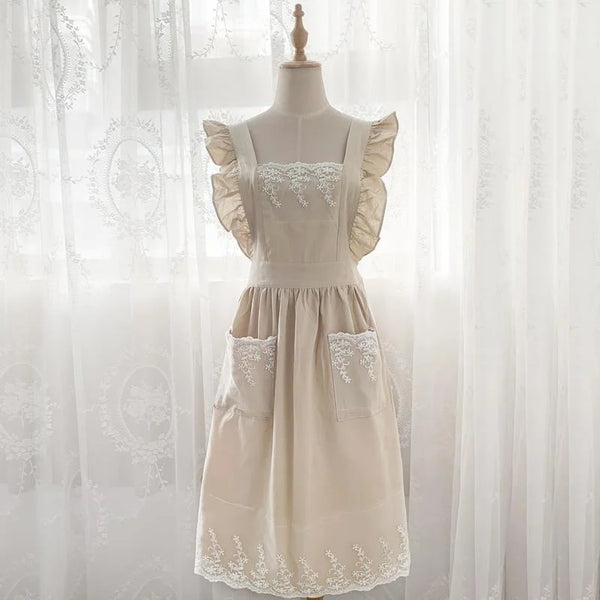 A cream linen kitchen apron with lace detailing and ruffled sleeves displayed on a mannequin.