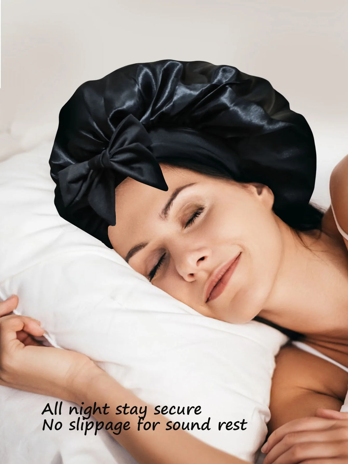 A woman wearing a black silky satin sleep bonnet rests peacefully on white bedding.