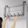 A hand is installing an over-the-door organizer rack with extended arms onto a white door frame.