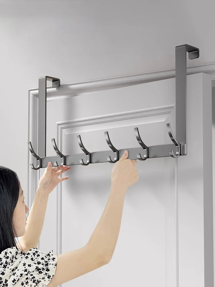 A hand is installing an over-the-door organizer rack with extended arms onto a white door frame.