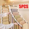 A hand is hanging folded beige pants on a multi-layer wooden hanger system with white non-slip clips.