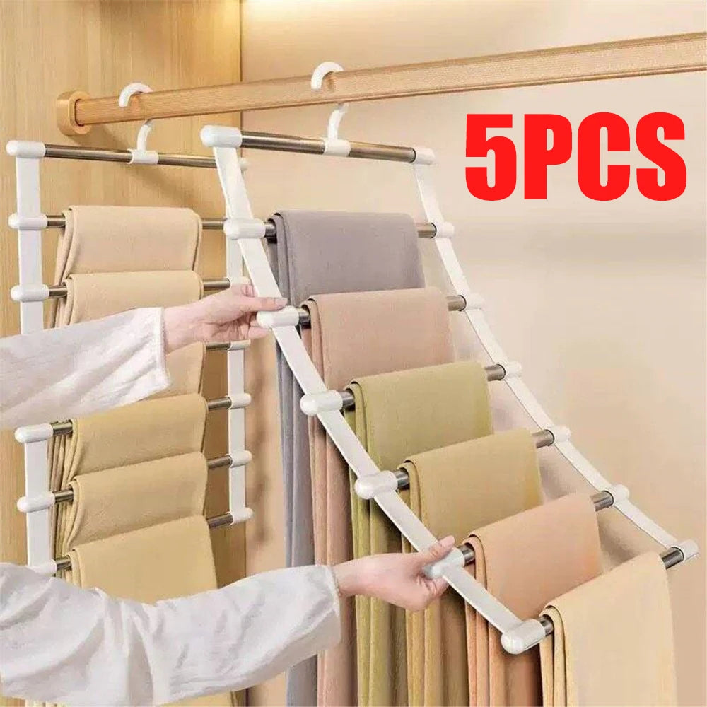 A hand is hanging folded beige pants on a multi-layer wooden hanger system with white non-slip clips.