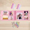 Álbum de scrapbooking rosa con páginas estampadas coloridas y pegatinas decorativas sobre una superficie de madera.