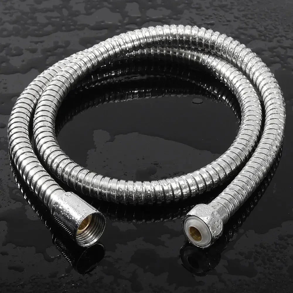 A coiled flexible stainless steel shower hose lying on a dark, reflective surface.