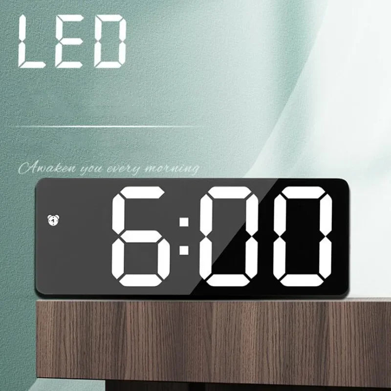 A black LED digital clock displaying 6:00 on a wooden surface.