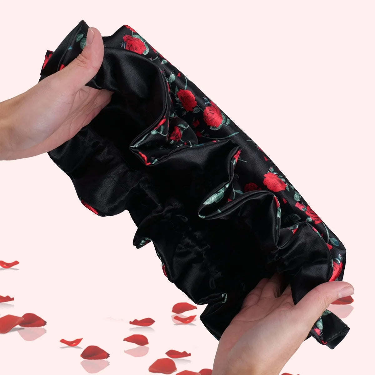 A hand is holding a black satin sleeping bonnet with a floral print, showing the fabric's texture and design.