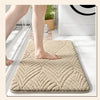 A beige plush non-slip bathroom rug is shown on a white floor next to a bathtub.