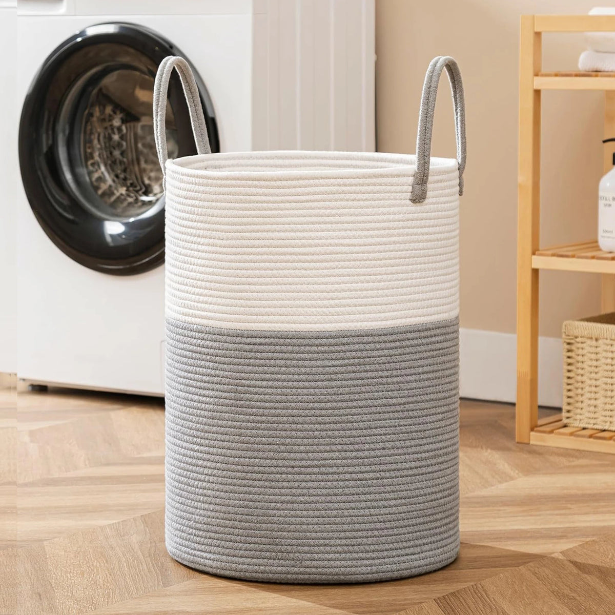 A large woven storage hamper with handles in white and gray stripes sits on a wooden floor next to a washing machine.