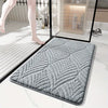 A gray plush non-slip bathroom rug is shown on a white floor next to a glass panel.