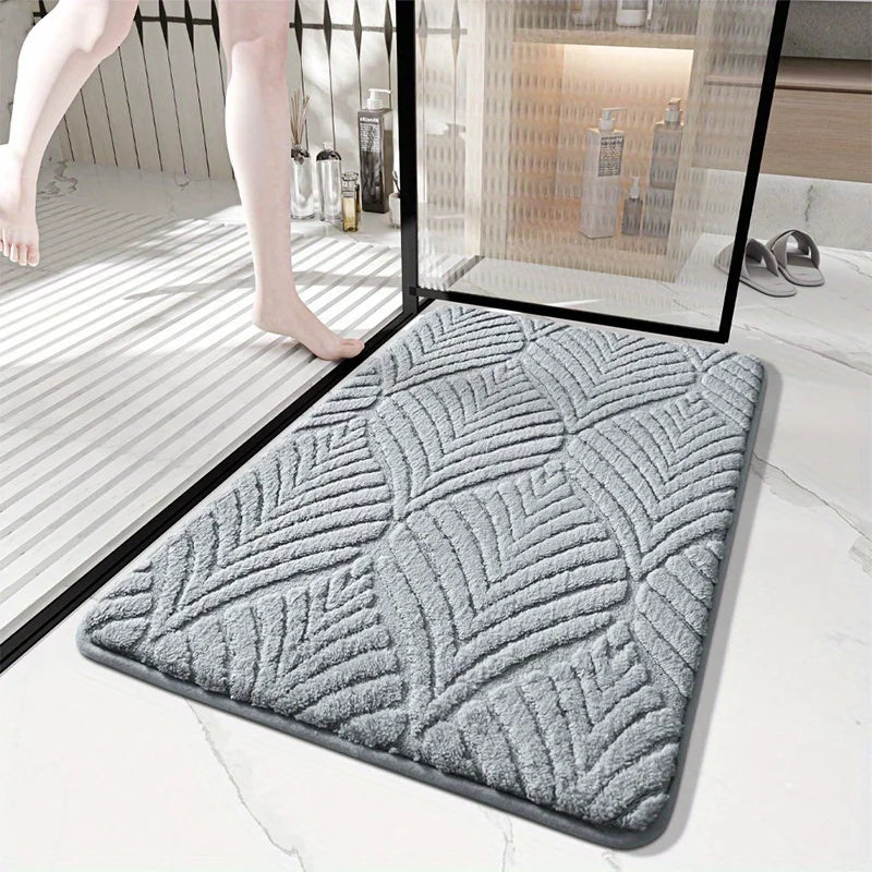 A gray plush non-slip bathroom rug is shown on a white floor next to a glass panel.