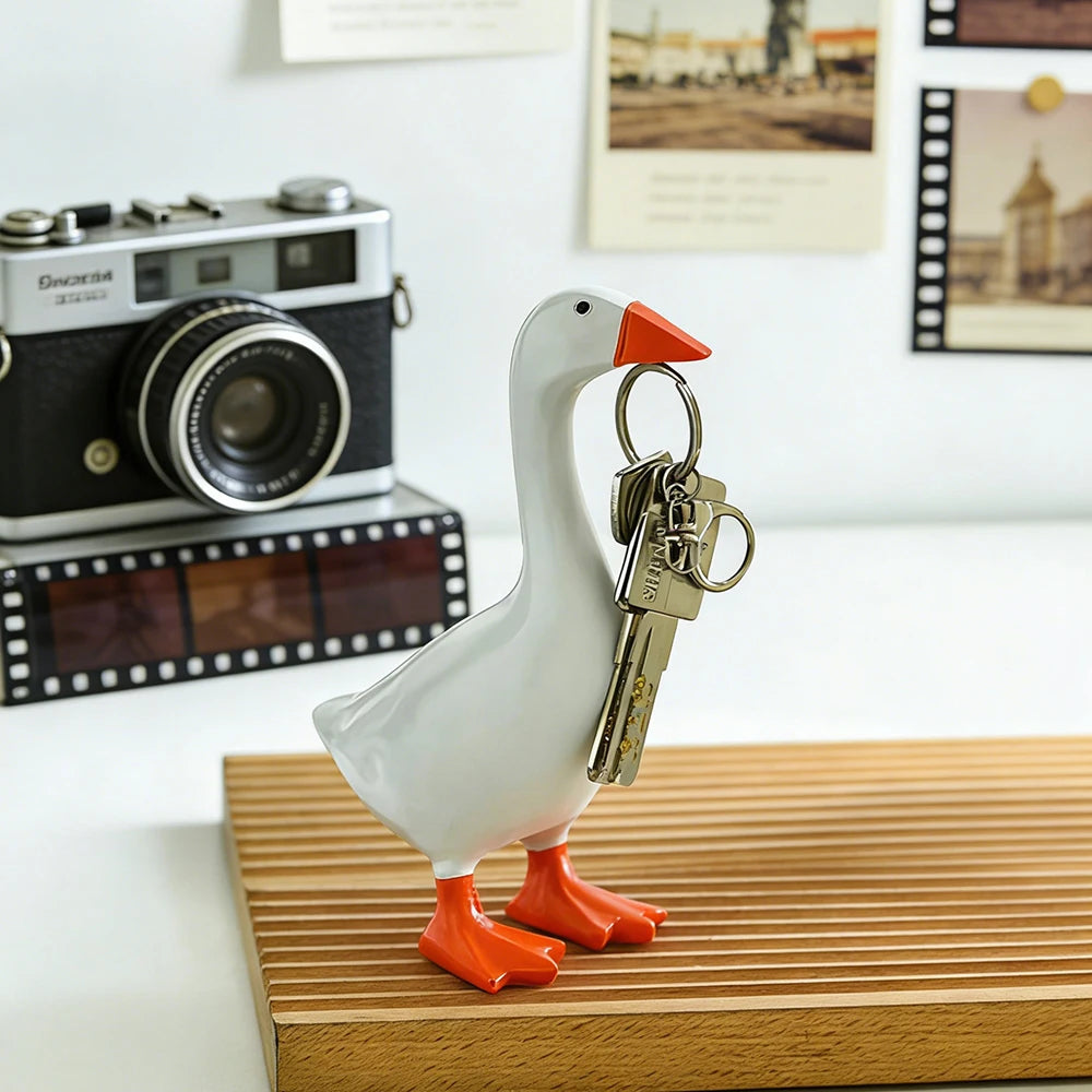 A white goose sculpture with orange feet holds a brass key chain.