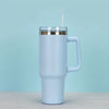 A white insulated stainless steel tumbler with a handle and straw set against a light blue background.