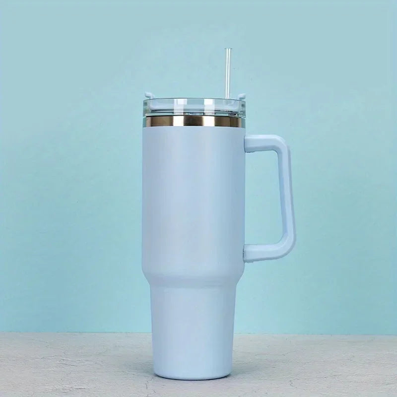 A white insulated stainless steel tumbler with a handle and straw set against a light blue background.