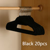 Black velvet slim hangers with metal hooks hanging from a wooden rod.