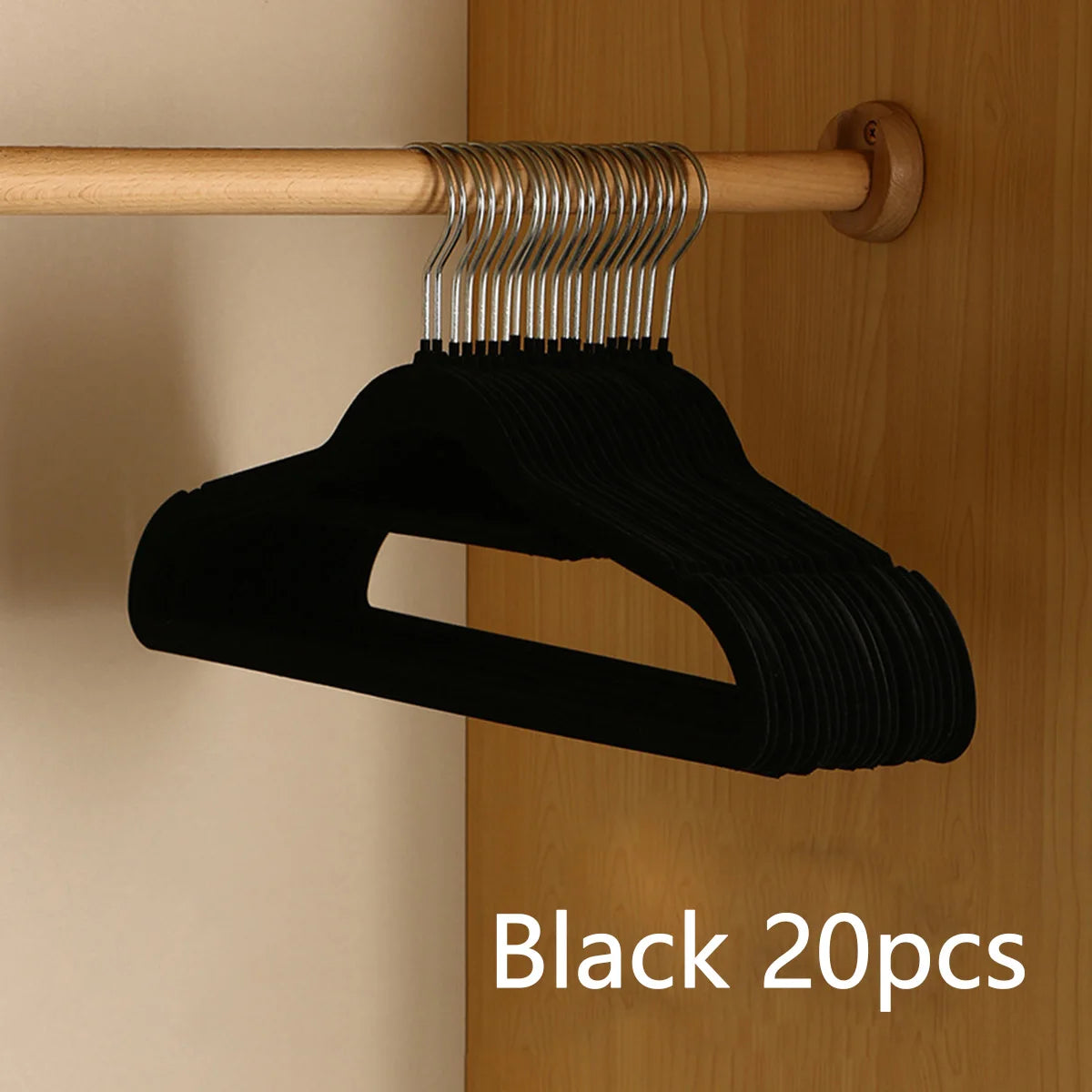 Black velvet slim hangers with metal hooks hanging from a wooden rod.