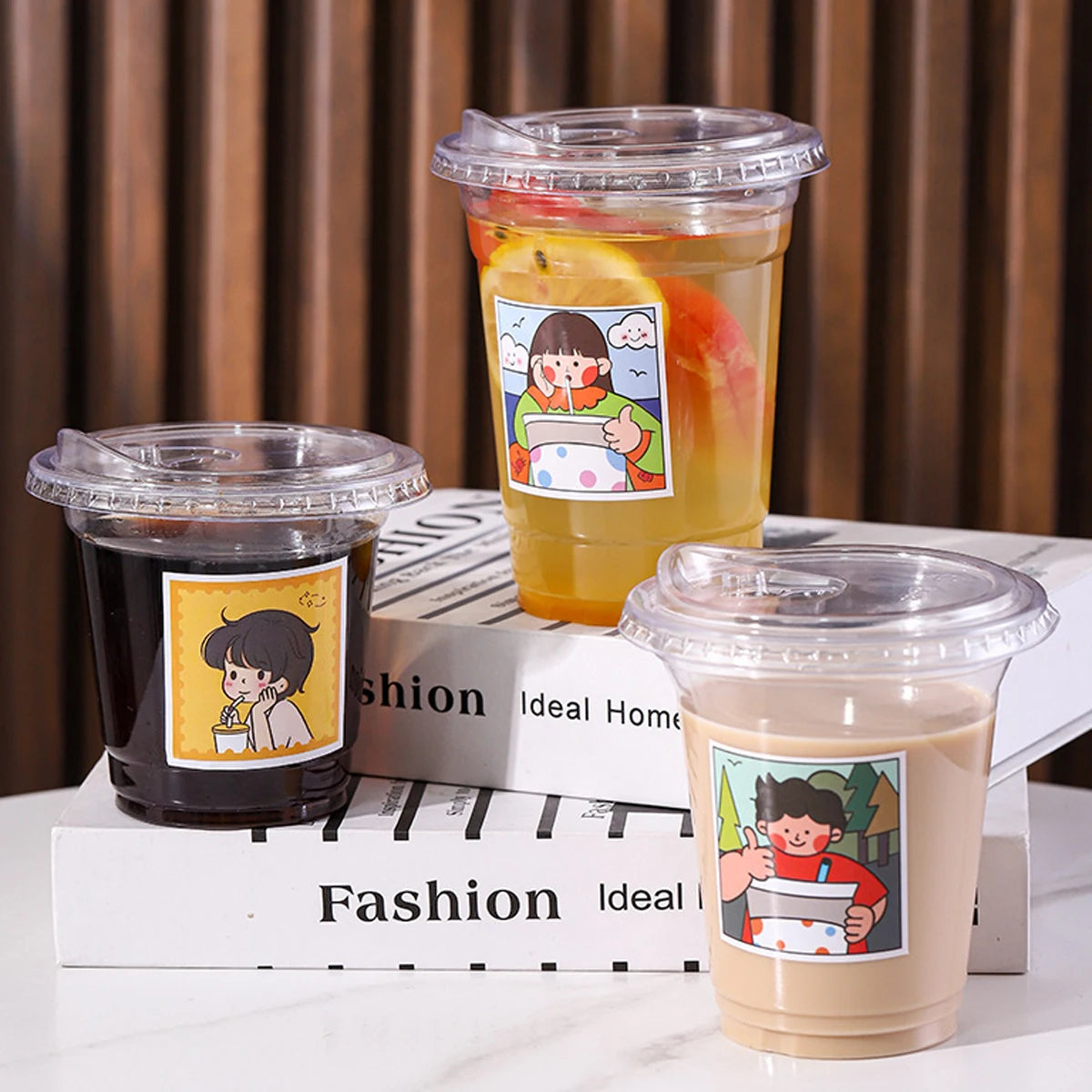 Two clear disposable coffee cups filled with different colored beverages are displayed on a stack of books.