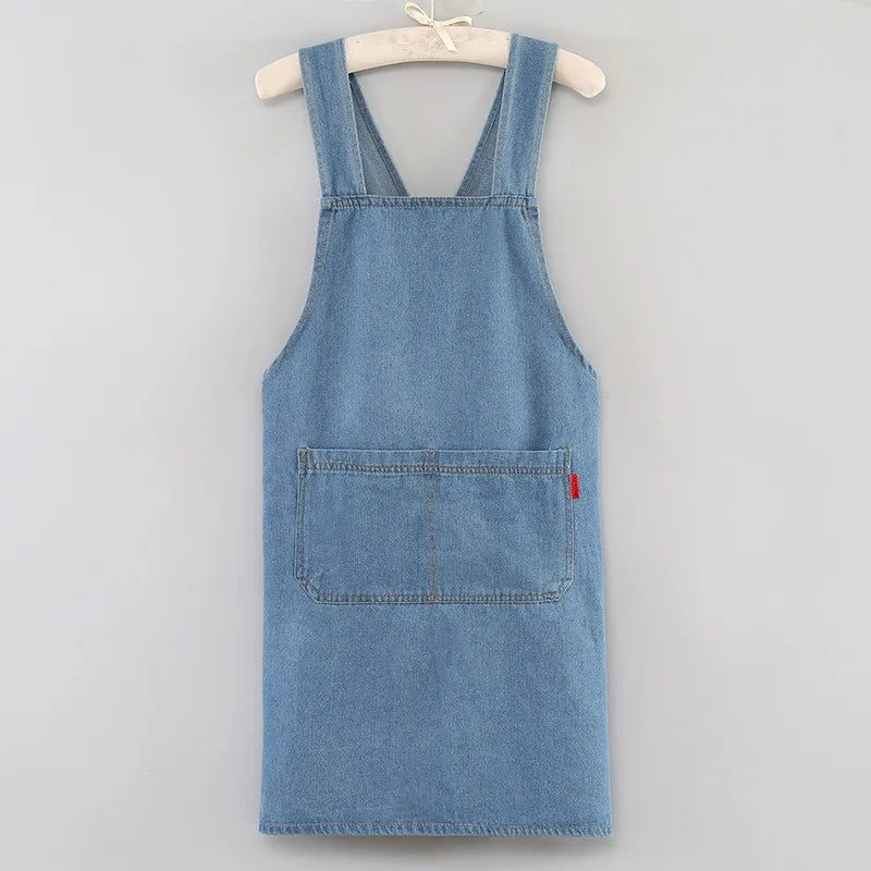A denim apron with a bib front and patch pocket is displayed on a hanger.