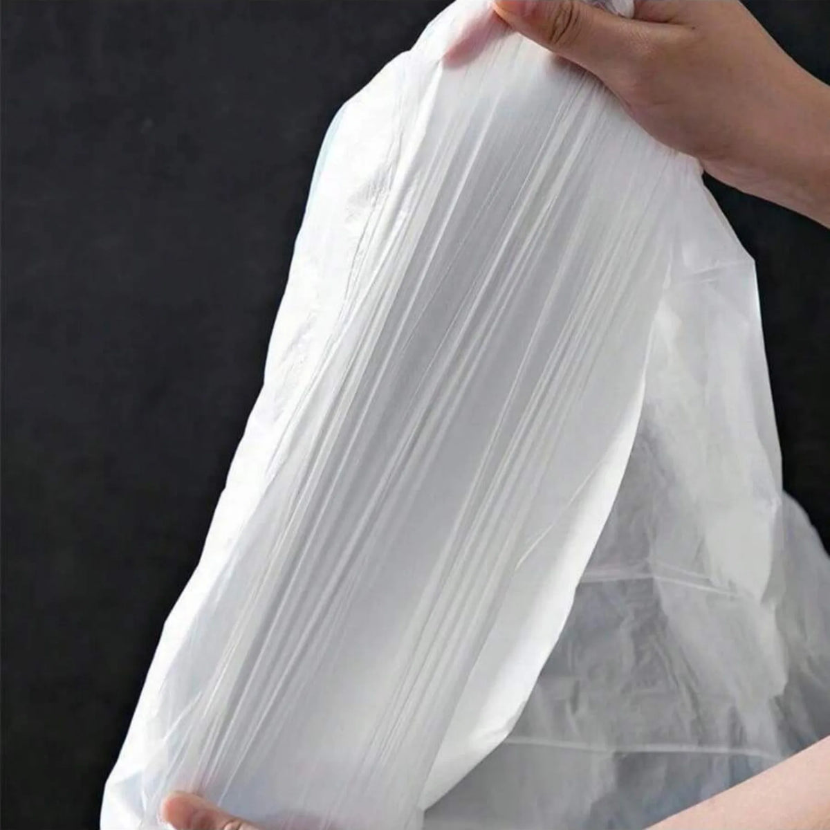 A hand is holding a clear white plastic drawstring trash bag.
