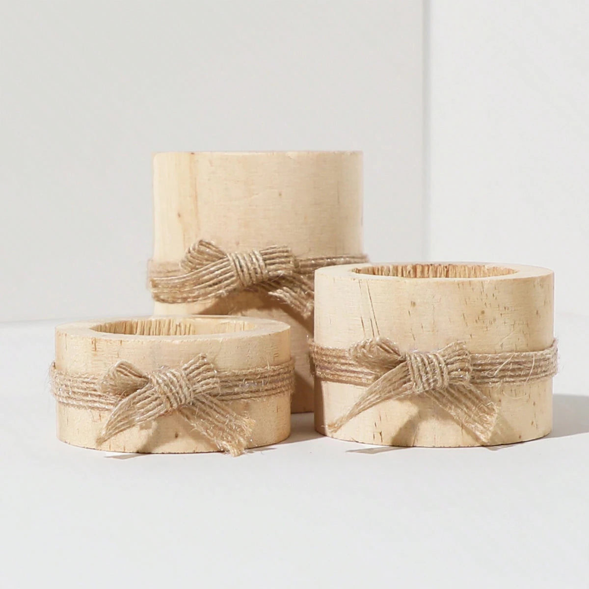 Tres portavelas de té de madera natural atados con cuerda sobre una superficie blanca.
