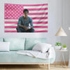 A man sits in front of a patriotic American flag tapestry featuring red, white, and blue stripes and stars.