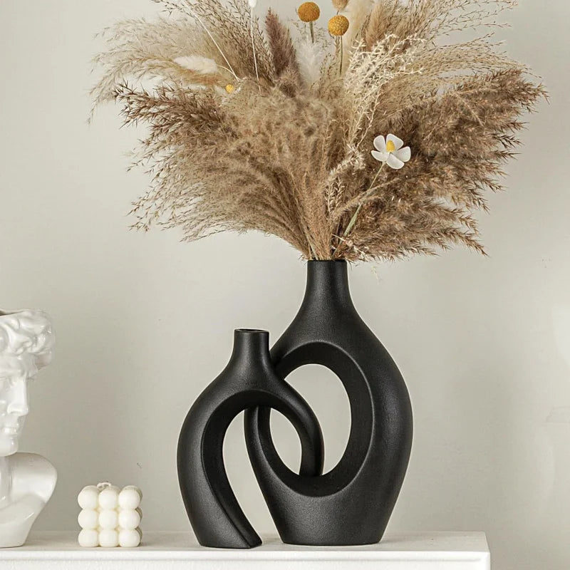 A black ceramic vase holds a dried floral arrangement of feathery beige grasses and small yellow flowers.