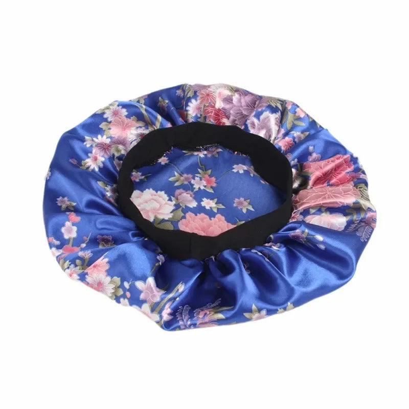 A satin sleep bonnet in blue with a floral print and a black elastic band.