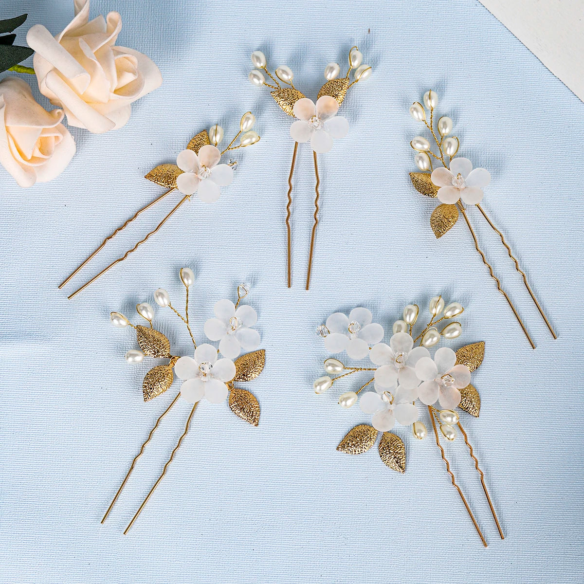 A set of delicate pearl and gold floral bridal hair clips arranged on light blue fabric.
