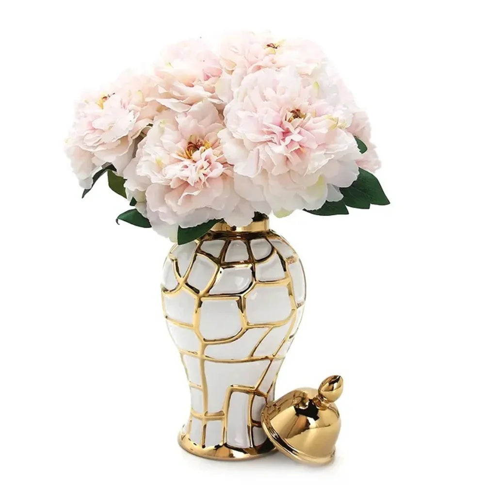 A golden and white ceramic flower vase holding a bouquet of light pink flowers.