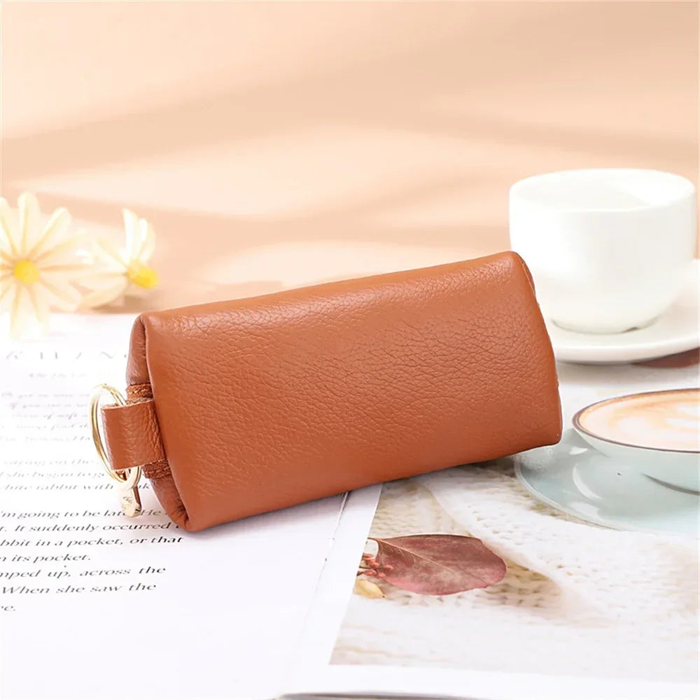 A brown leather key organizer wallet with a zipper closure resting on a white surface next to a cup of coffee.