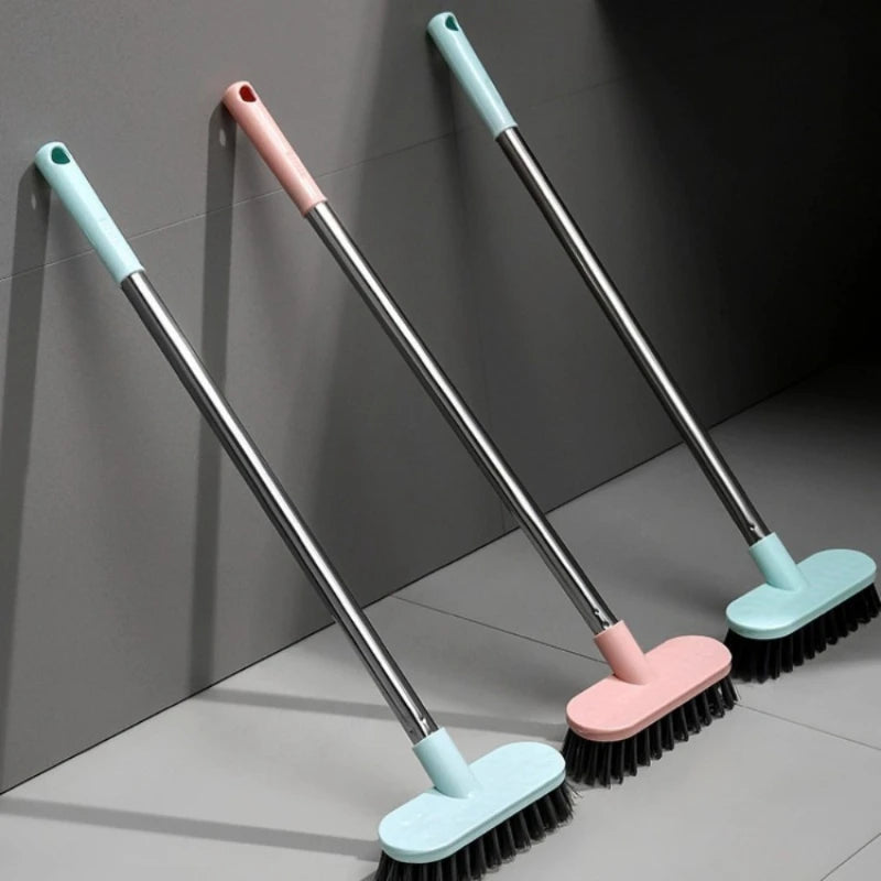Three long-handle floor scrub brushes in light blue and pink are shown against a gray wall.