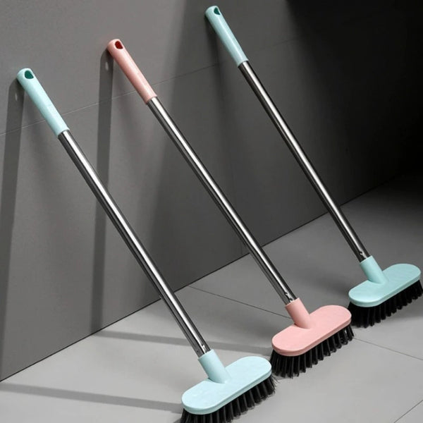 Three long-handle floor scrub brushes in light blue and pink are shown against a gray wall.