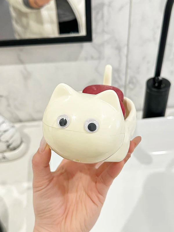 A hand holds a cute cat-shaped soap dish with a drainage rack, featuring white and reddish-pink colors.