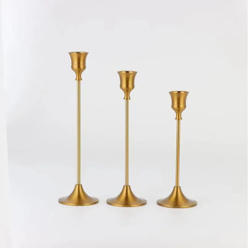 A set of three elegant brass metal candle holders with slender stems and flared bases.