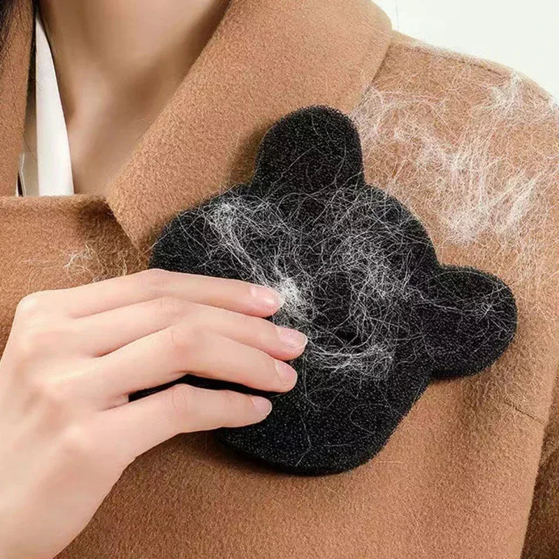 A hand holds a black reusable pet hair remover sponge against a brown coat.