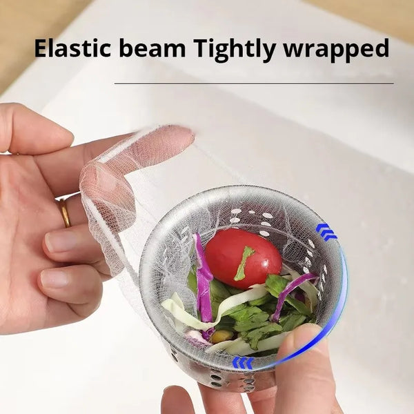 A hand holds an elastic beam tightly wrapped disposable sink drain filter bag containing leafy greens and a tomato.