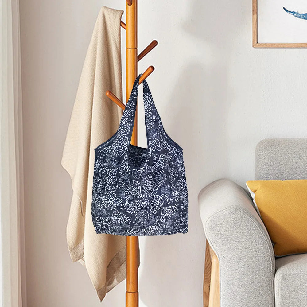Dunkelblaue gemusterte wiederverwendbare Tasche hängt an einem Holzständchen neben einem beigen Handtuch.