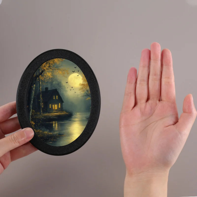 A round, black photo frame featuring a silhouette of a house reflected in water under a glowing moon and trees.