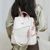 A woman is holding a white and pink PU leather travel backpack against a light background.