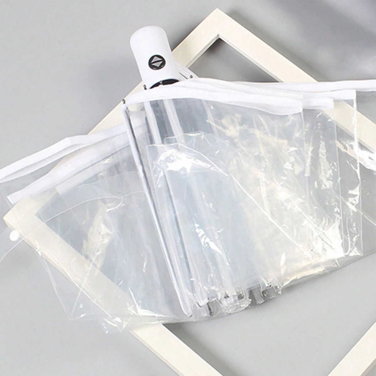A white automatic transparent folding umbrella is shown folded within a light wooden frame.