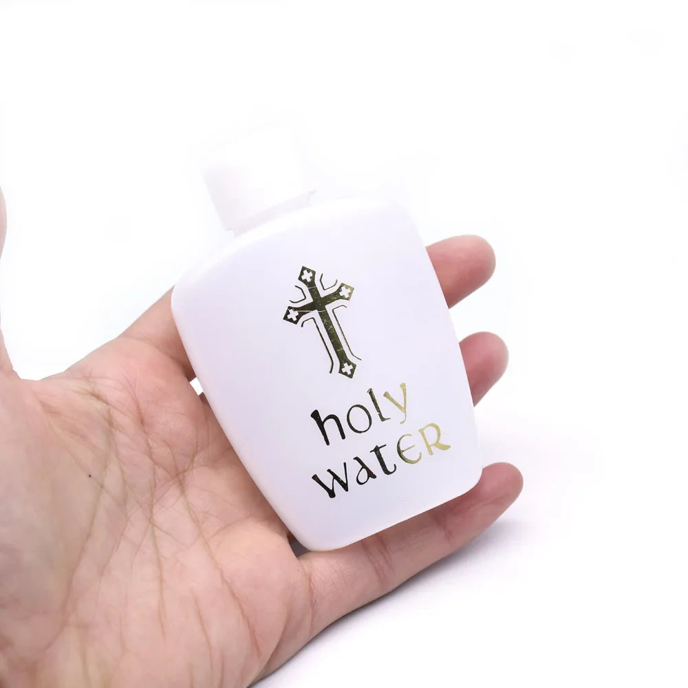 A white bottle of holy water with a cross design is held in a hand against a white background.