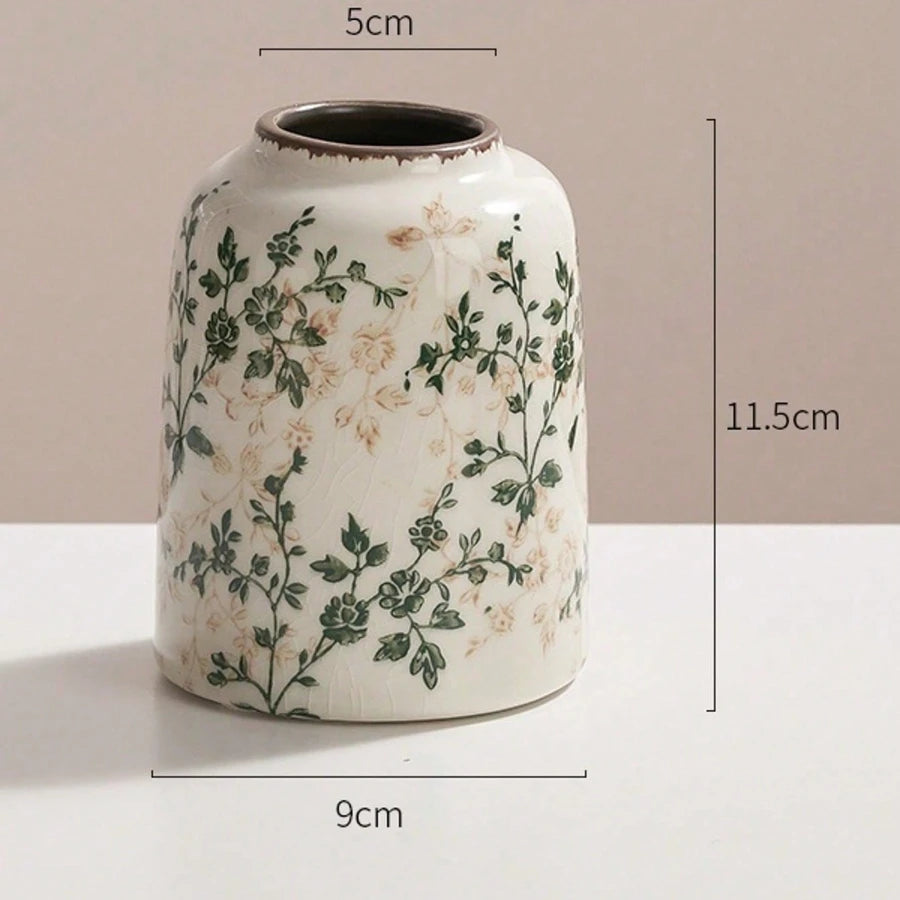 A white ceramic bud vase with a dark rim and green floral pattern, shown against a neutral background.
