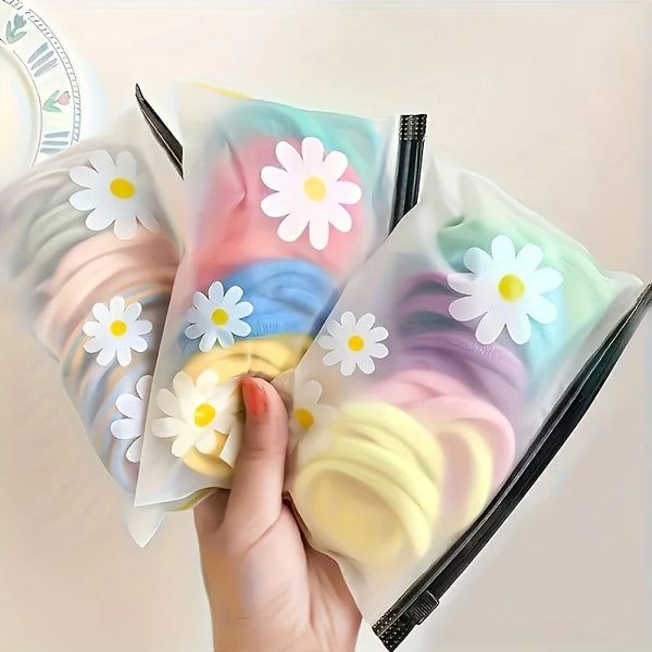 A hand holds a clear plastic storage bag filled with pastel pink and yellow silicone daisy pattern fabric for organizing item