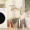 A white washing machine next to a woven basket holding gray towels and stainless steel adhesive hooks on a light-colored wall