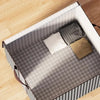 A foldable clothing storage bag with a gray and white checkered pattern is shown open on a wooden floor.